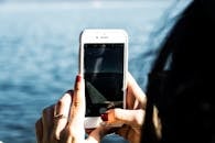 Close-up of a person photographing a serene lake using a smartphone, showcasing technology in nature.